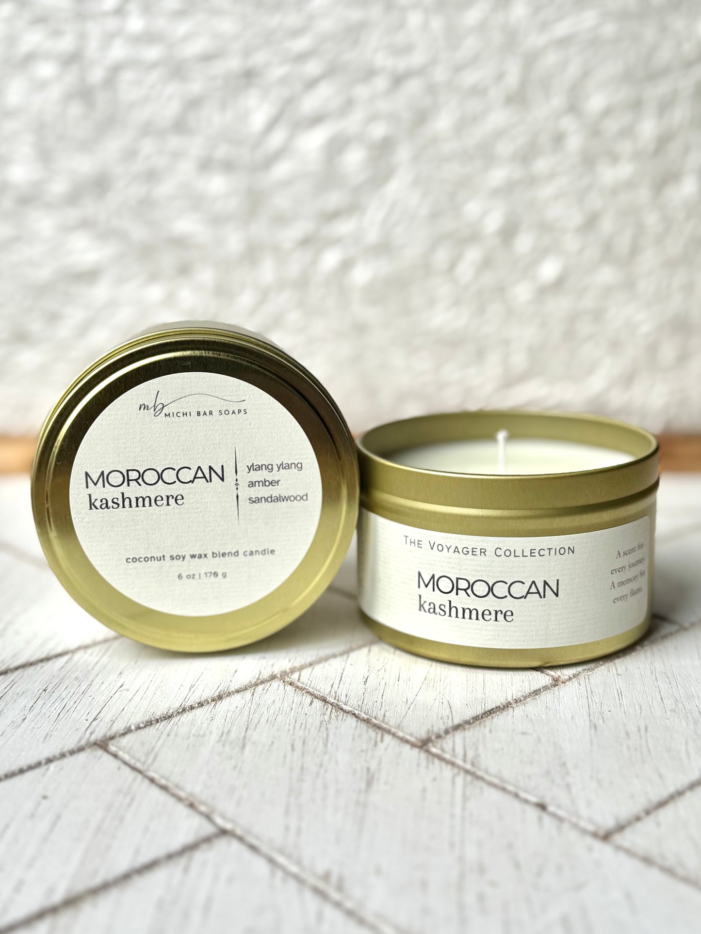 A gold-colored tin candle with the label 'Moroccan Kashmere' in white text, placed on a wooden surface with a white background.