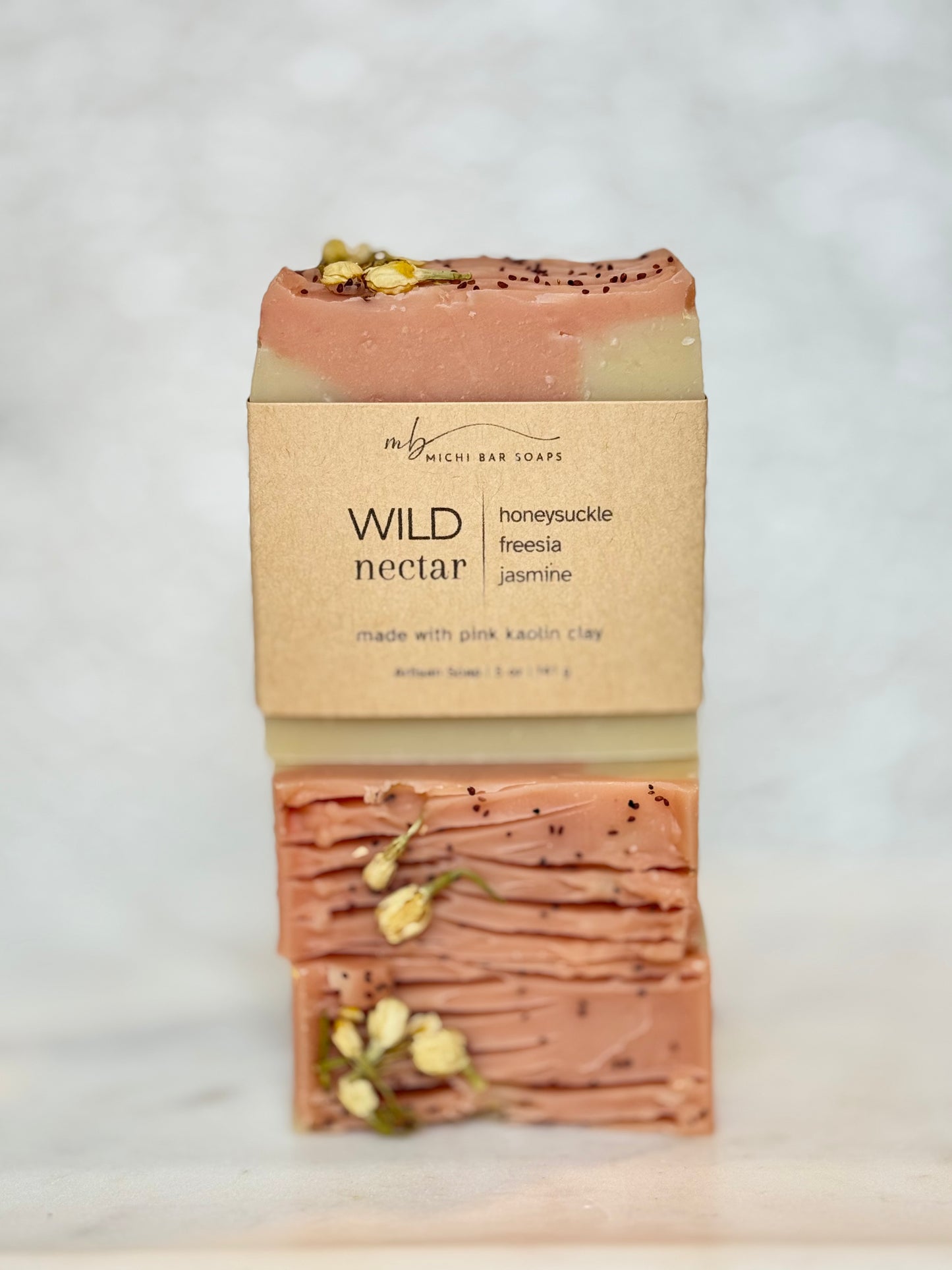 A single bar of soap from the brand 'my precious bar soaps' named 'WILD nectar', wrapped in a kraft paper sleeve, standing vertically on a light marble surface against a white marble background.