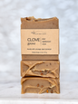 Three stacked bars of artisan soap with a kraft paper label reading 'CLOVE grove' and 'MICHI BAR SOAPS,' photographed on a light marble surface against a soft white marble background.