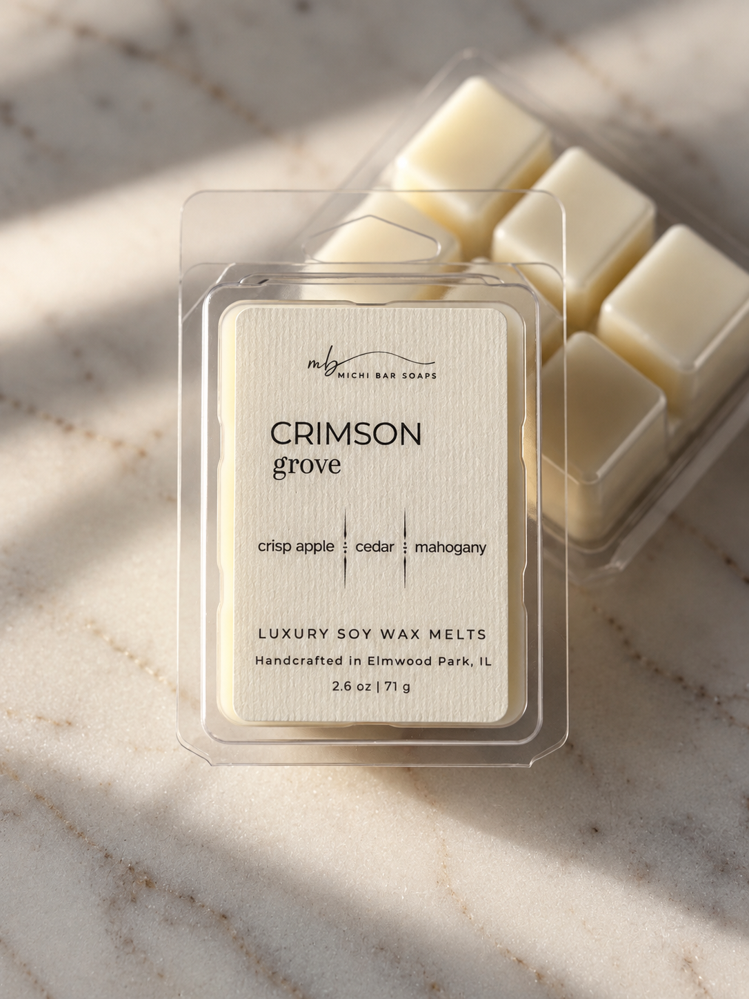 Wax melts in a clear plastic clam shell with a cream label that says 'Crimson Grove' with scent notes of crisp apple, cedar and mahogany leaning against another wax filled clam shell