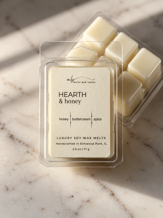A clear plastic clamshell package of luxury soy wax melts labeled 'HEARTH & honey' sits on a light marble surface, with additional wax melts visible behind it.