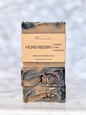 Two stacked handmade bar soaps with a kraft paper label reading 'HONEYBERRY' and 'michi bar soaps,' photographed on a light marble-like surface against a soft white marble background.