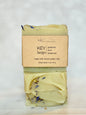 A bar of handmade soap labeled 'KEY largo' by Rich Bar Soaps, featuring a light yellow-green base with blue dried flower accents, wrapped in a kraft paper label on a light marble surface.