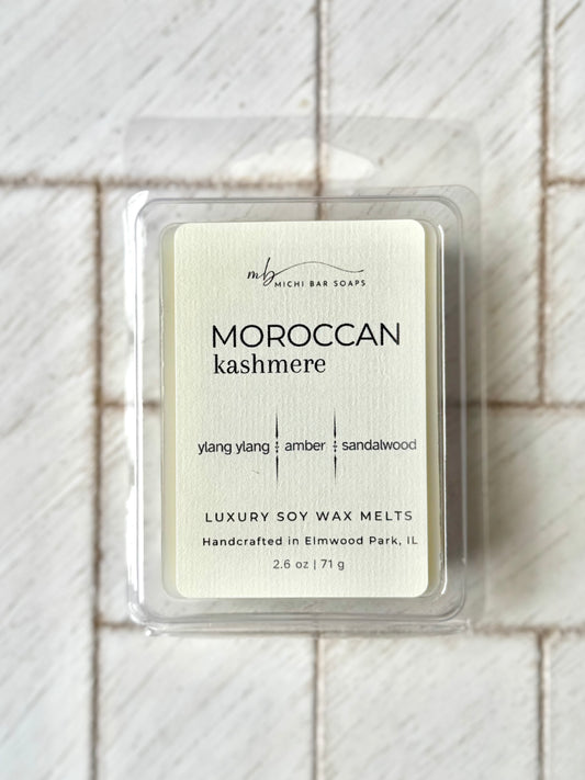 A package of Moroccan Kashmere wax melts, displayed on a white surface. The packaging is predominantly white with product name and scents listed on it.