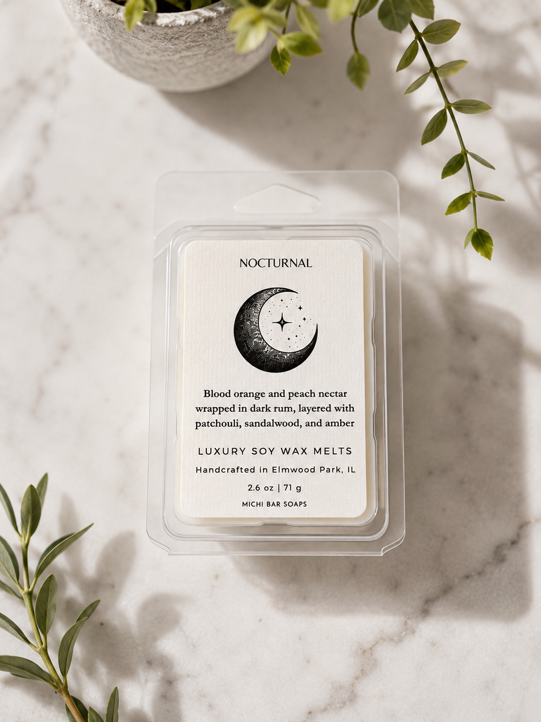 A clear plastic clamshell package of Nocturnal soy wax melts sits on a light marble surface with green leaves and a small plant in the background. The label reads 'NOCTURNAL' and 'Blood orange and peach nectar wrapped in dish rum, layered with patchouli, sandalwood, and amber.