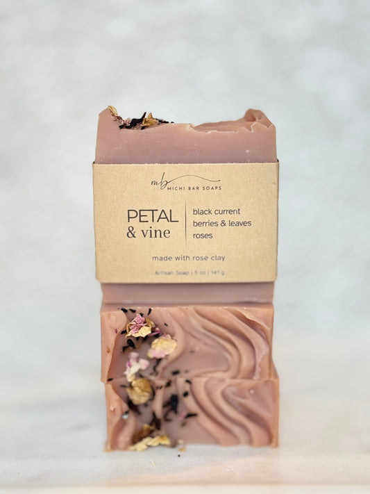 A handmade bar of soap labeled 'PETAL & VINE' by Richi Bar Soaps, featuring a dusty rose clay body with visible dried flower petals and leaves, set against a light marble background.
