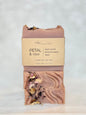 A handmade bar of soap labeled 'PETAL & VINE' by Richi Bar Soaps, featuring a dusty rose clay body with visible dried flower petals and leaves, set against a light marble background.
