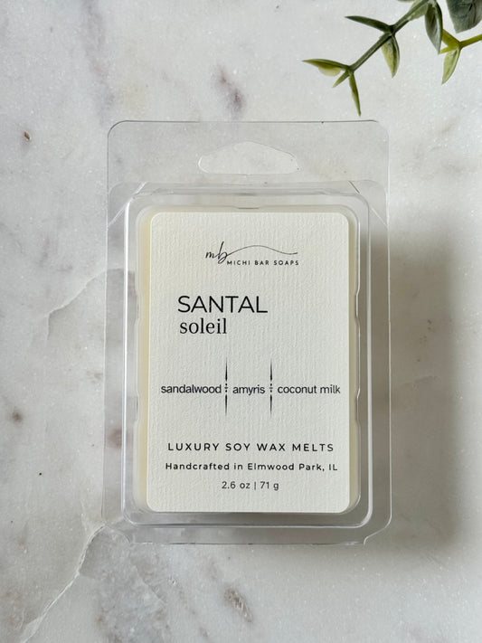 Pack of 'Santal Soleil' soy wax melts on a marble surface with a plant leaf.