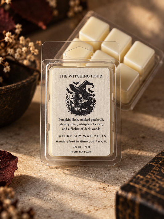 A clear plastic clamshell package of 'The Witching Hour' luxury soy wax melts sits on a textured stone surface, with a second package of unopened wax melts in the background and dried autumn leaves and a dark wood bowl around it.