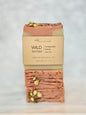 A single bar of soap from the brand 'my precious bar soaps' named 'WILD nectar', wrapped in a kraft paper sleeve, standing vertically on a light marble surface against a white marble background.