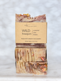 Three stacked bars of artisan soap with a kraft paper label reading 'WILD bouquet' and 'michi bar soaps,' photographed on a light marble surface against a soft white marble background.