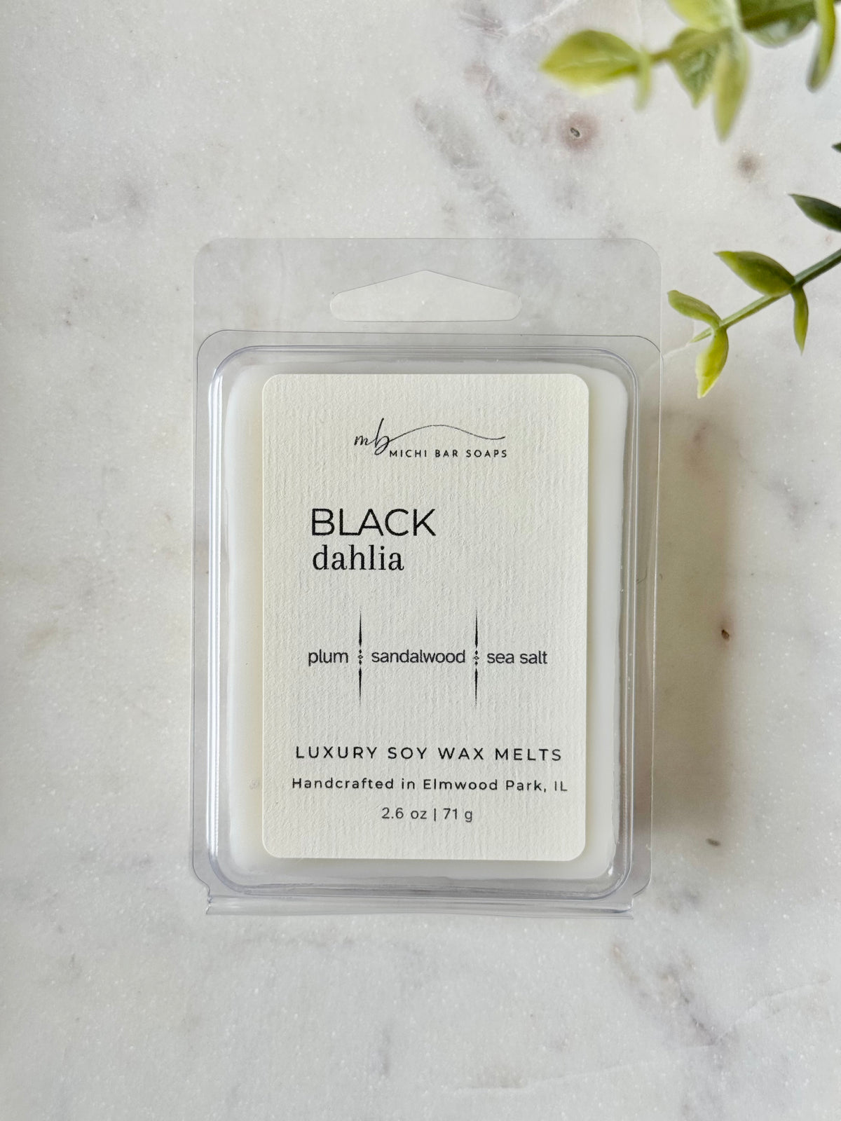 Pack of Black Dahlia soy wax melts on a marble surface with a plant in the corner.