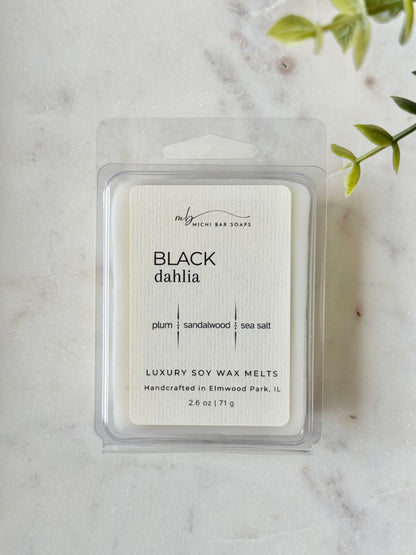 Pack of Black Dahlia soy wax melts on a marble surface with a plant in the corner.