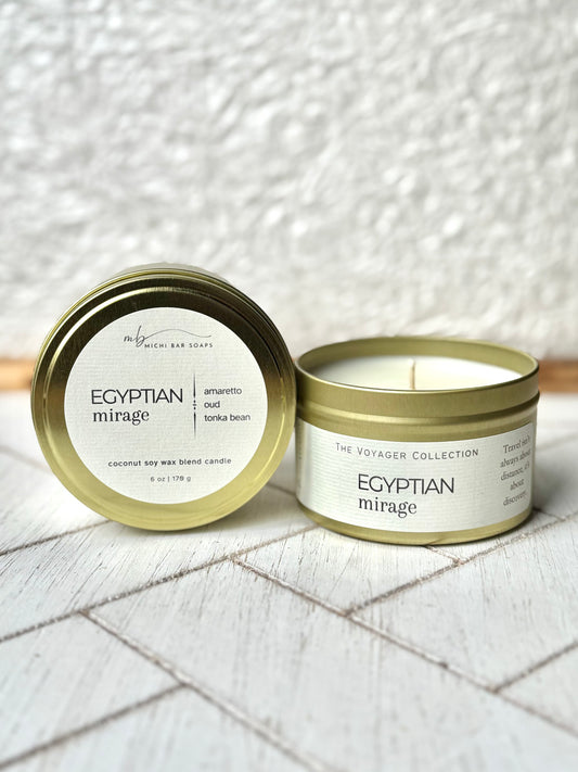 gold tin candles on a wood surface, labeled with cream labels that say Egyptian Mirage and scent notes of amareto,oud and tonka bean